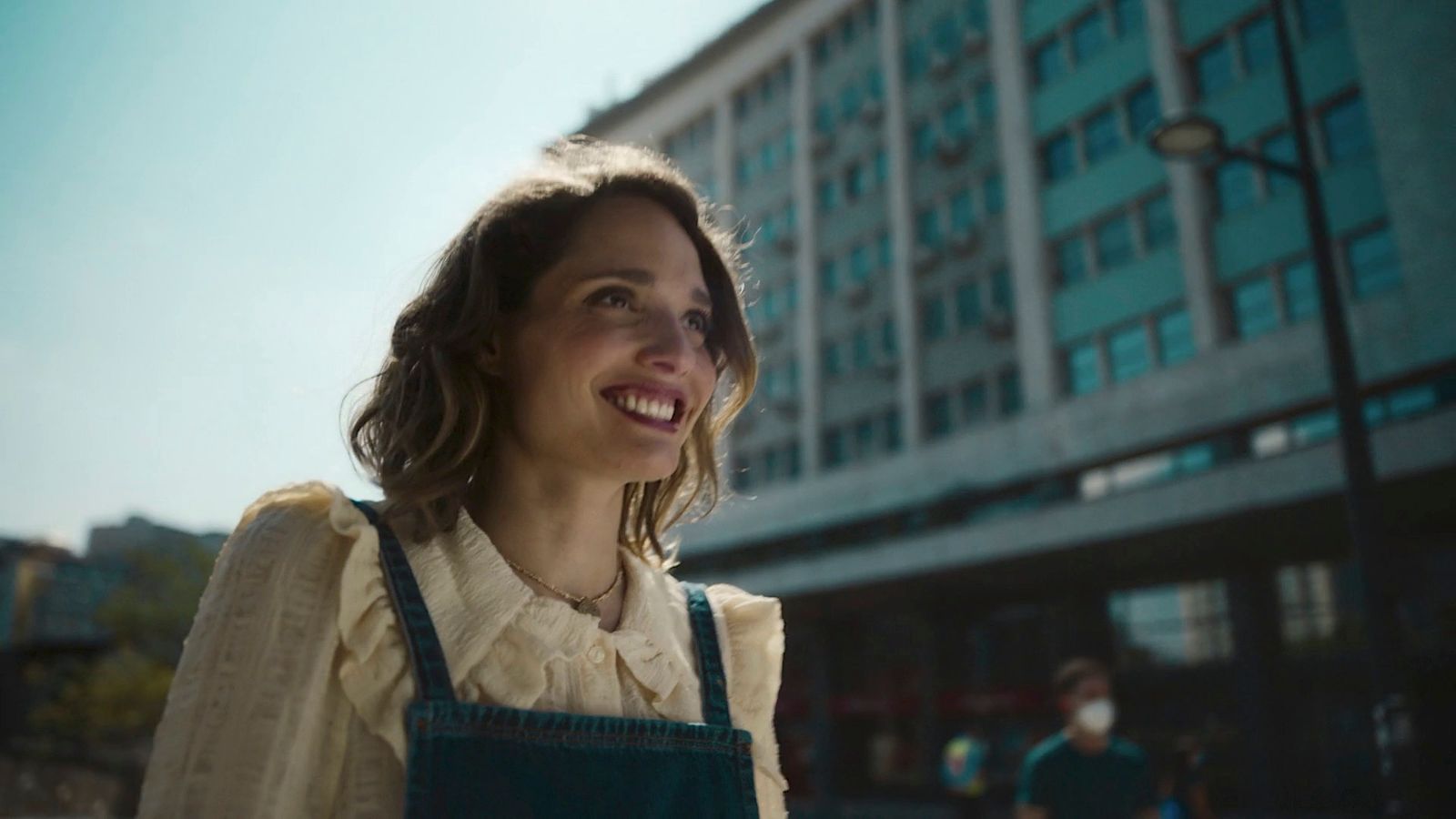 a woman in an apron smiles in front of a building