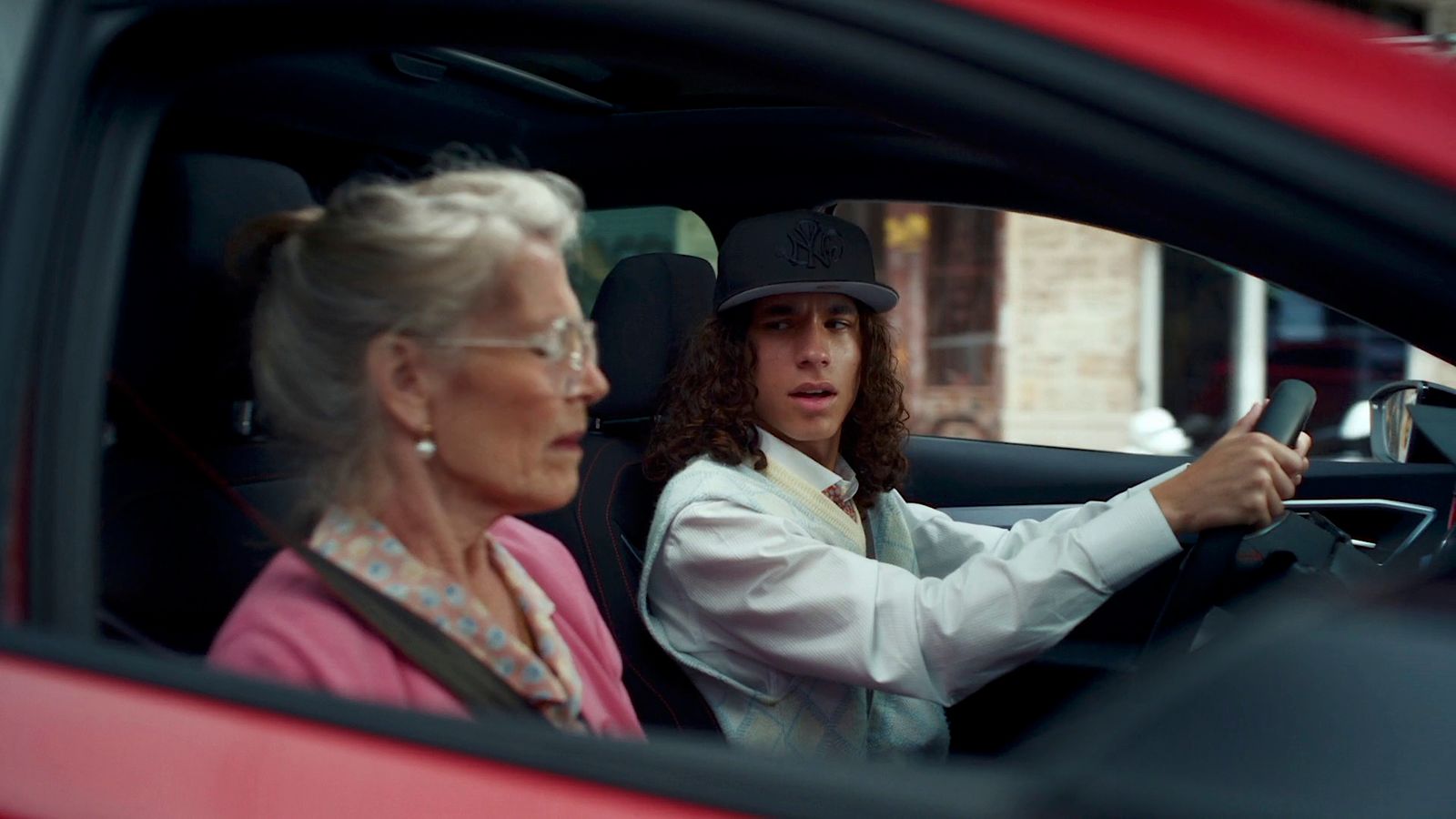 a woman driving a red car with a man in the driver seat