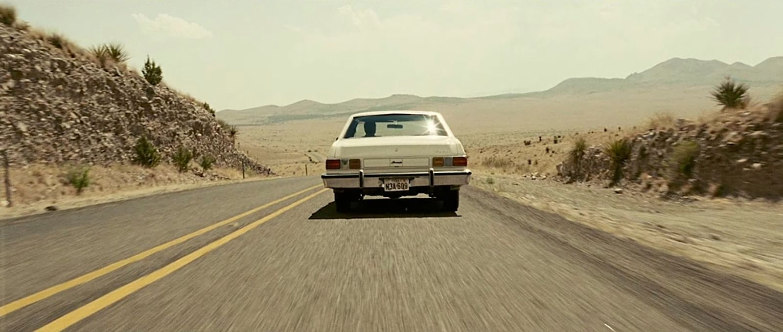 a white car driving down a desert road