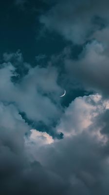 a cloudy sky with a half moon in the distance