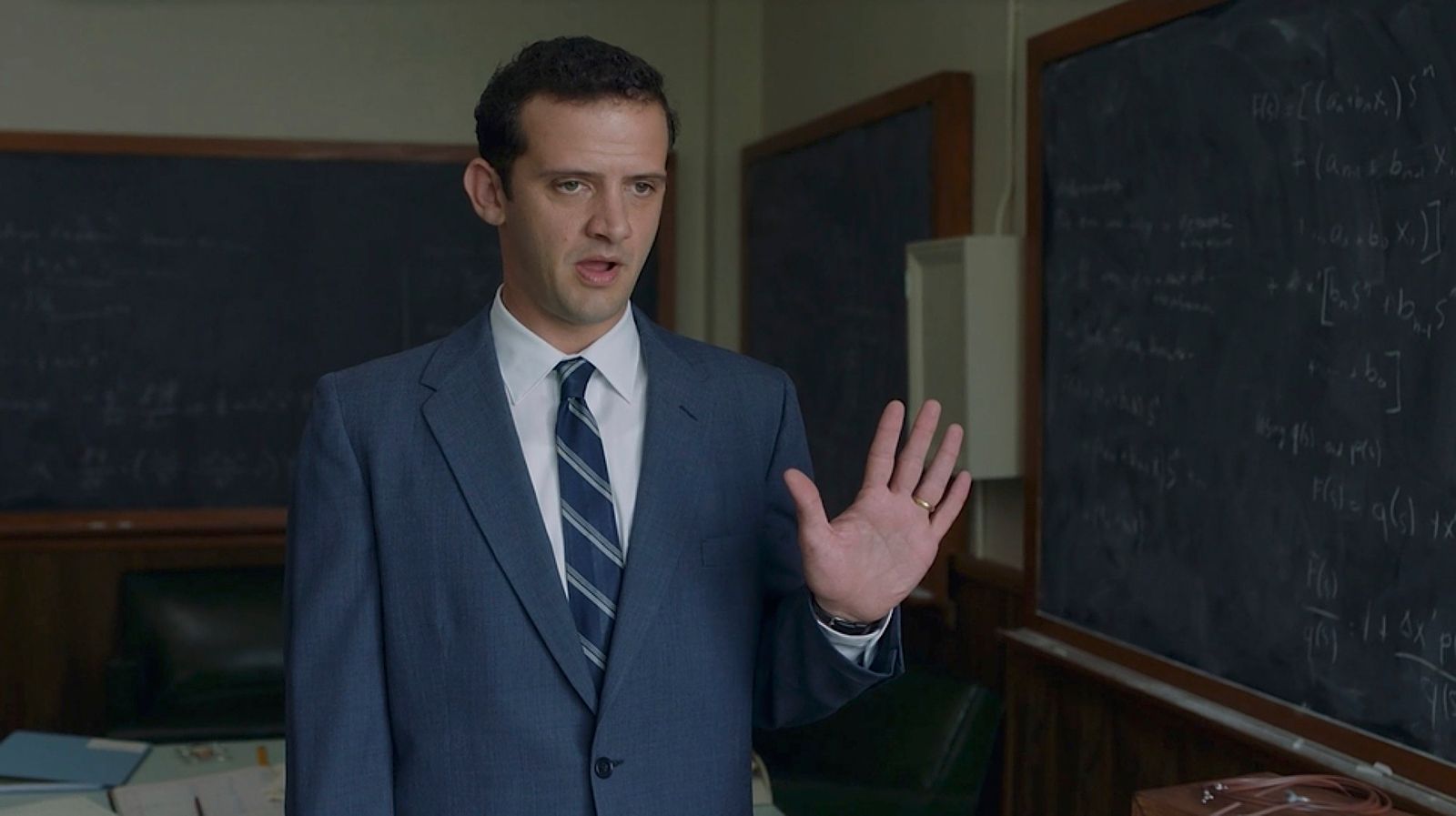 a man in a suit and tie standing in front of a blackboard