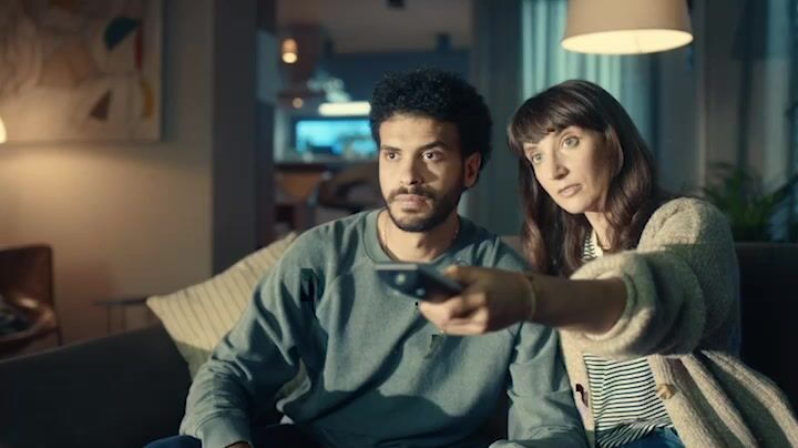 a man and a woman sitting on a couch holding remotes