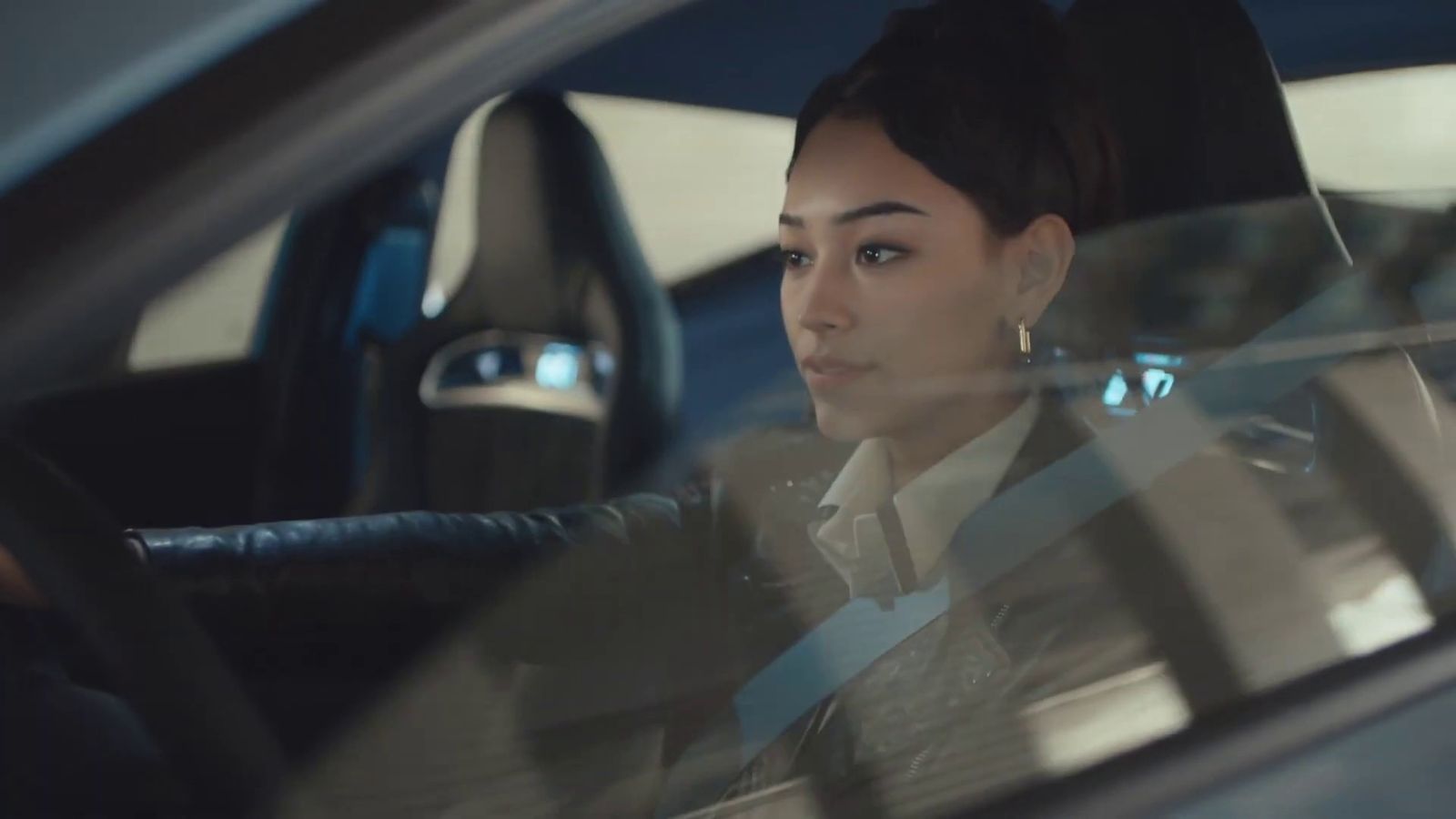 a woman sitting in a car with her hand on the steering wheel