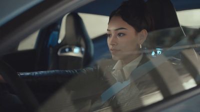 a woman sitting in a car with her hand on the steering wheel