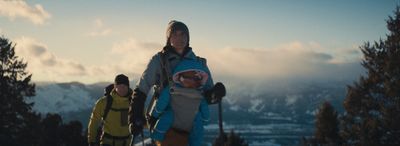 a woman holding a baby while standing on top of a snow covered slope