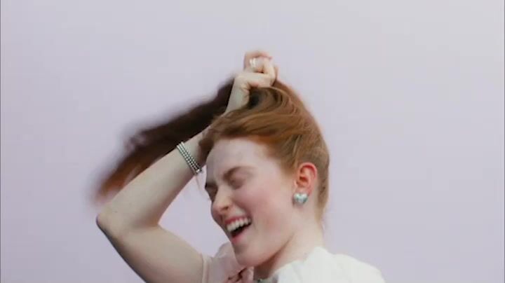 a woman with red hair is smiling and touching her hair