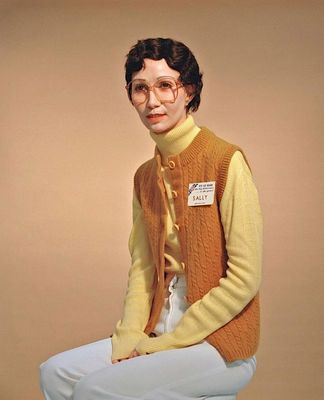 a woman sitting on a stool wearing a sweater and glasses