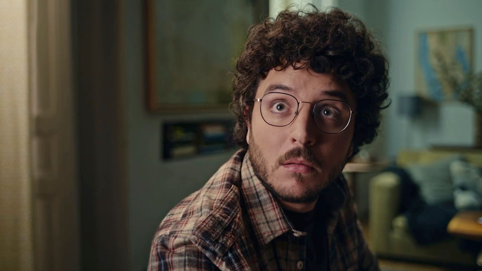 a man with curly hair and glasses making a face