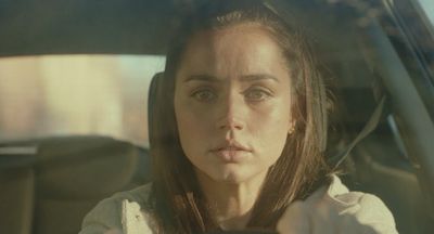 a woman sitting in a car with her hand on the steering wheel