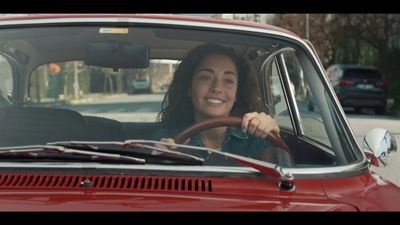 a woman driving a red car down a street