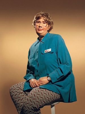 a woman sitting on a stool wearing a blue shirt and patterned pants