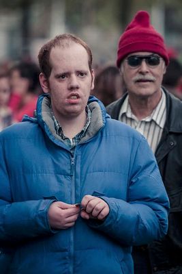 a man in a blue jacket standing next to a man in a red hat