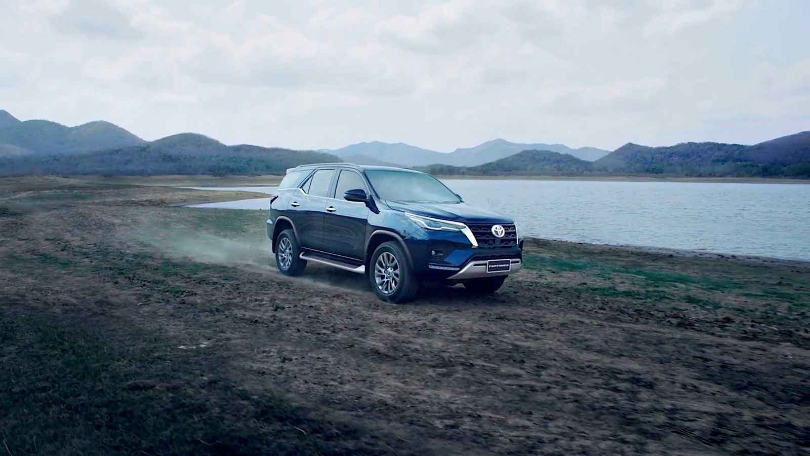 a blue suv driving down a dirt road next to a body of water