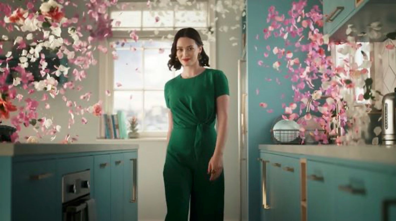 a woman in a green jumpsuit standing in a kitchen