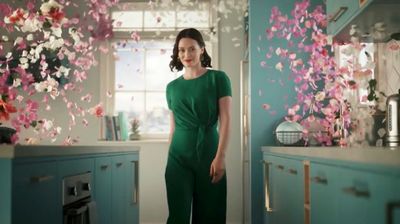 a woman in a green jumpsuit standing in a kitchen