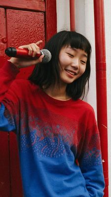 a young asian woman holding a microphone in front of a red door