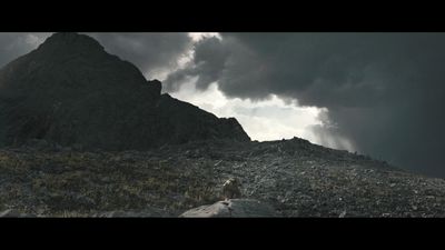 a man standing on top of a rocky hill under a cloudy sky