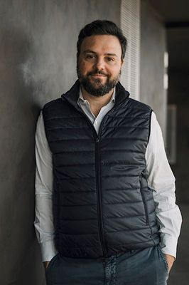 a man leaning against a wall wearing a vest