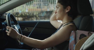 a woman sitting in a car with her hand on the steering wheel