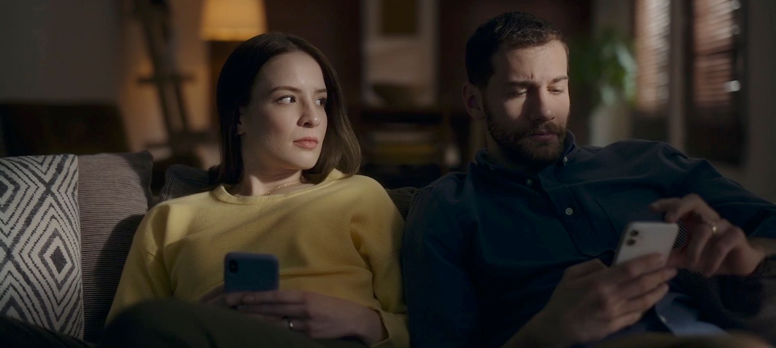 a man and a woman sitting on a couch looking at their cell phones