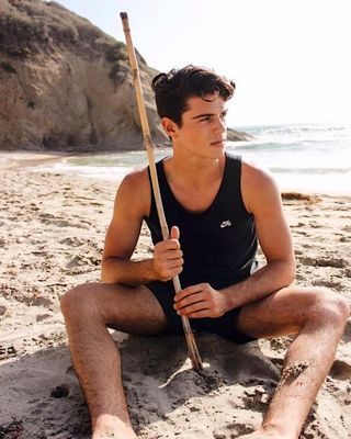 a man sitting on a beach holding a stick