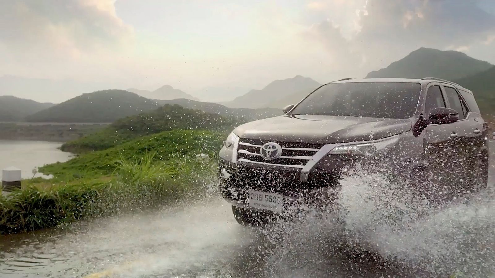 a black truck driving through a river next to a lush green hillside