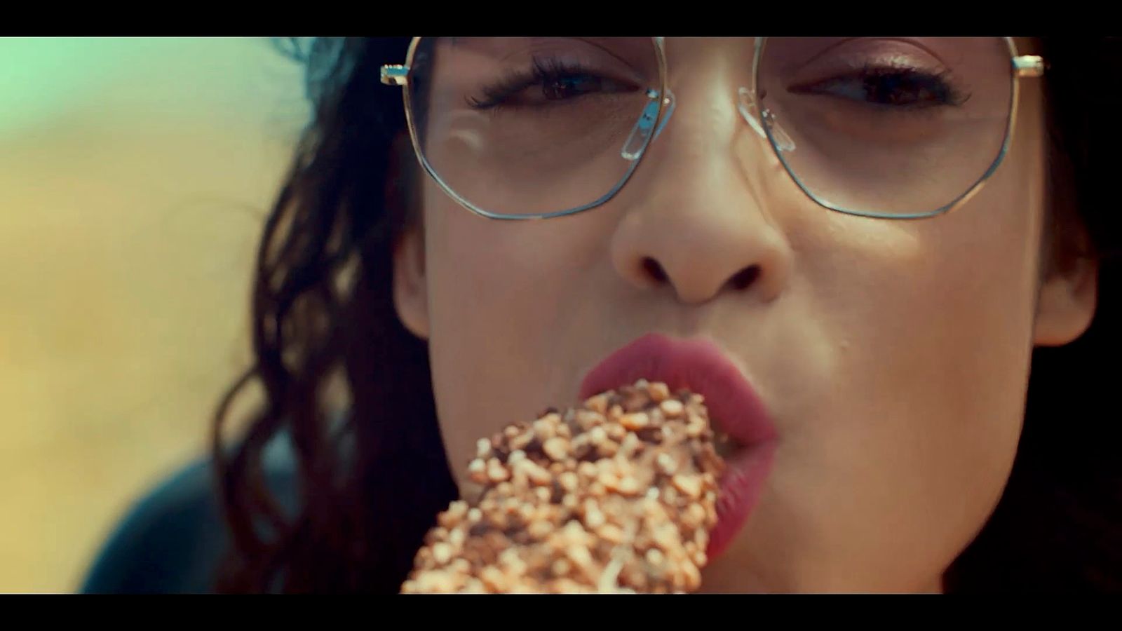 a woman wearing glasses eating a donut with sprinkles