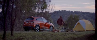 a red car parked next to a tent in the woods