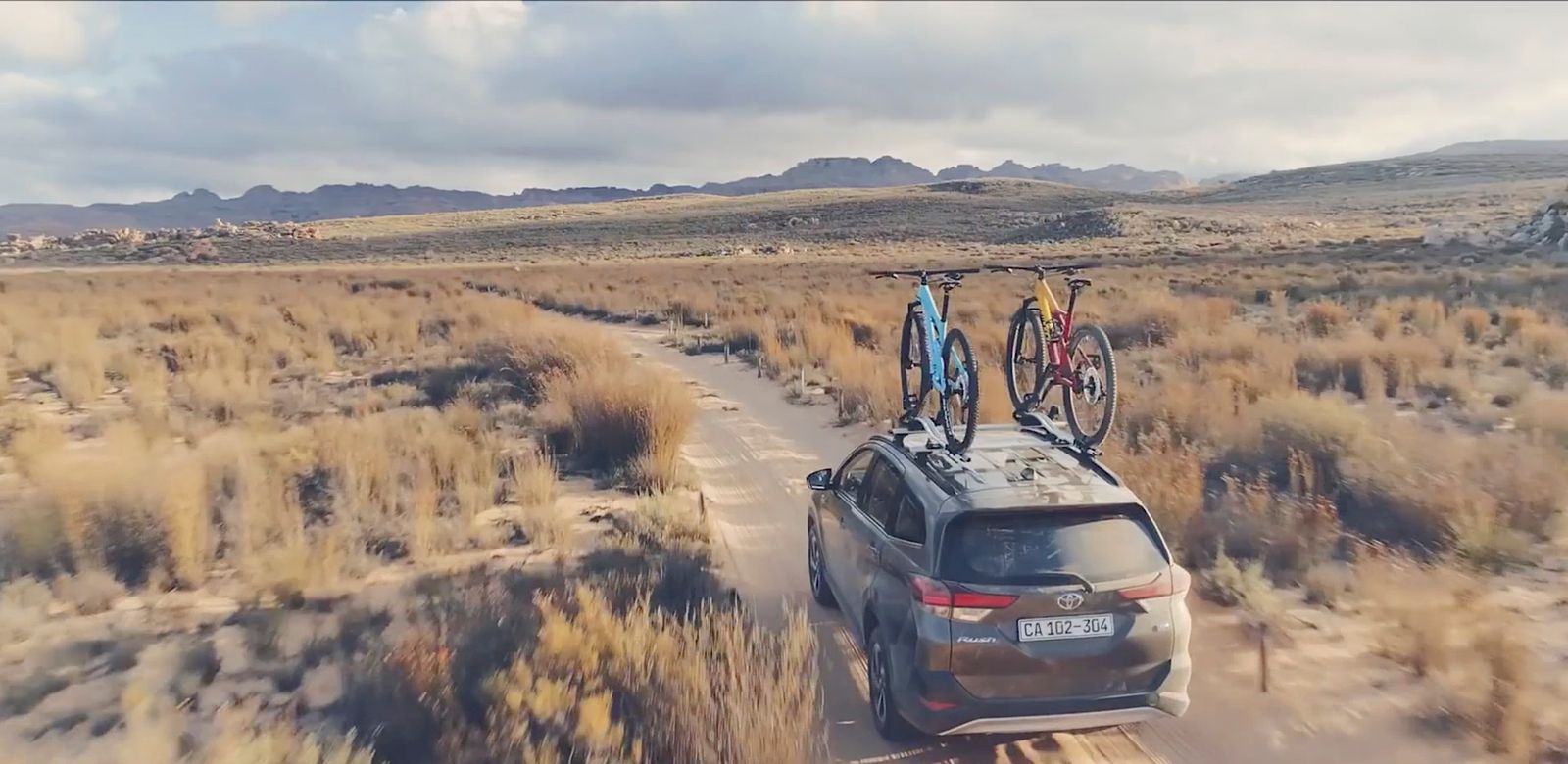 a car driving down a dirt road with a bike on top of it