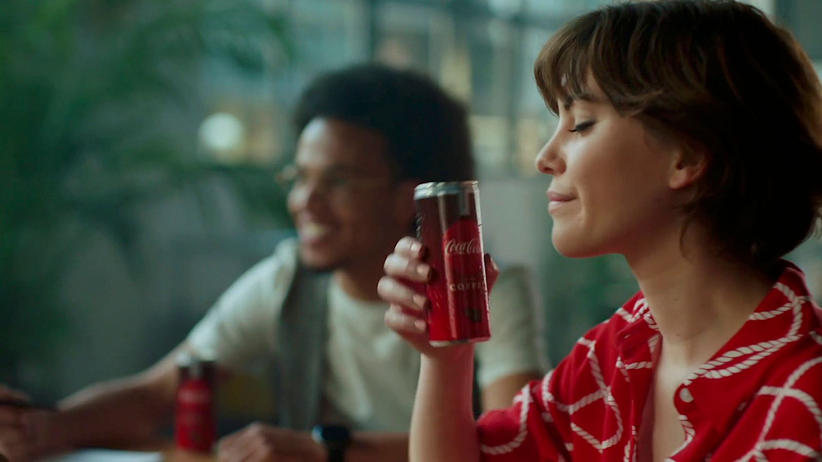 a woman sitting at a table holding a can of soda