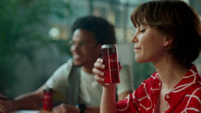 a woman sitting at a table holding a can of soda