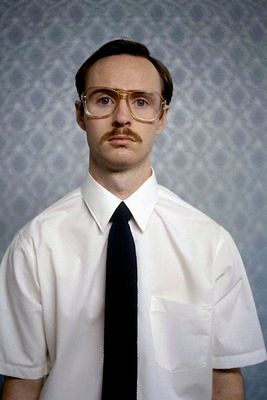 a man wearing glasses and a tie with a mustache