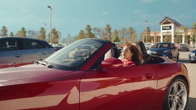 a woman driving a red convertible car in a parking lot