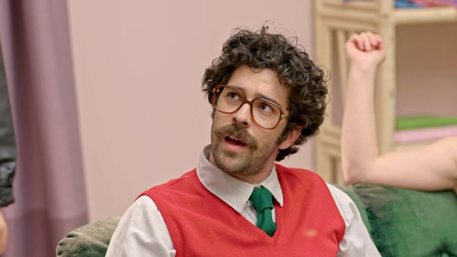 a man with curly hair wearing a red vest and green tie