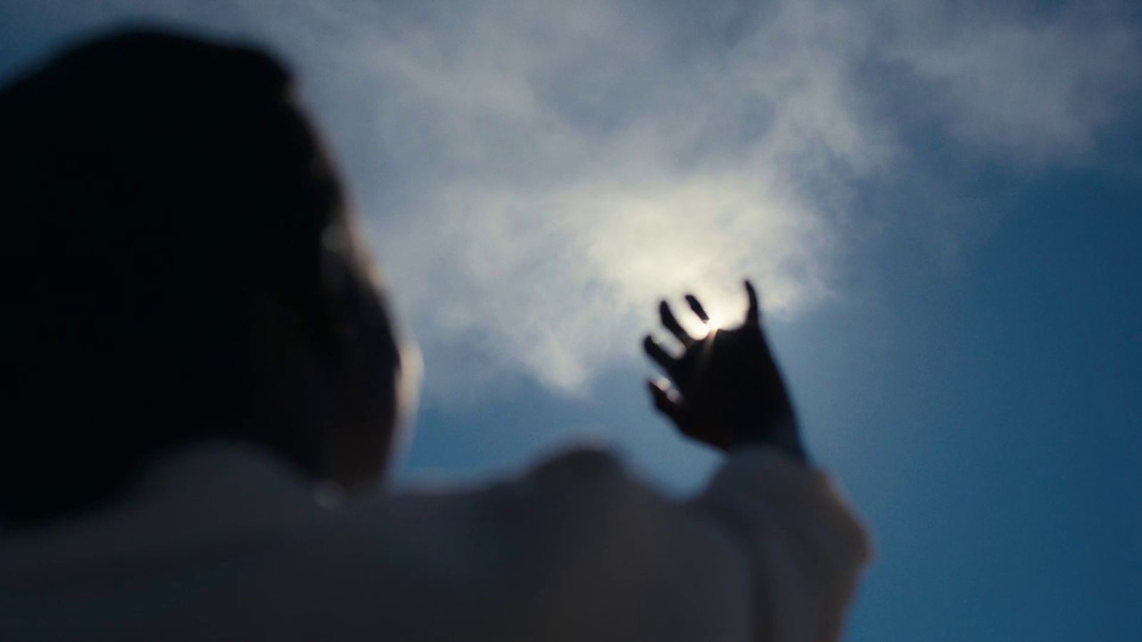 a silhouette of a person reaching up into the sky