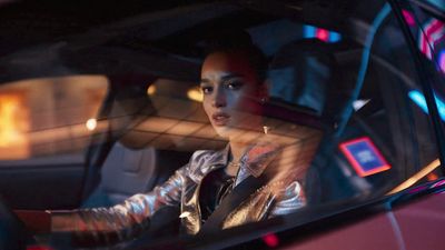 a woman sitting in a car with her hand on the steering wheel