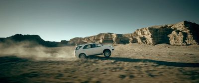 a white car driving through a desert with rocks in the background