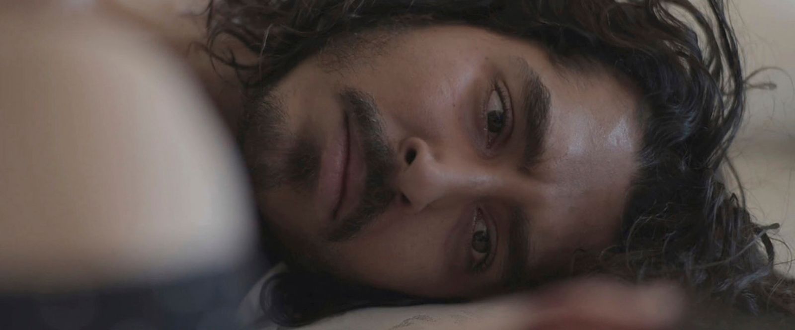 a man with long hair laying on a bed