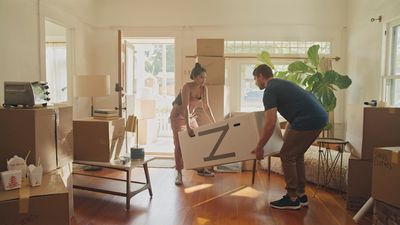 a man and a woman moving boxes into a house