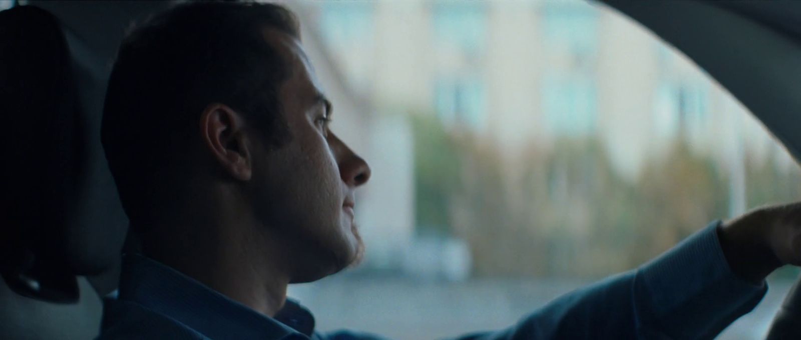 a man sitting in a car with his hand on the steering wheel