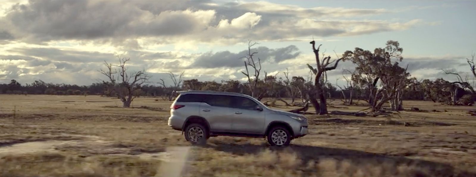 a silver truck driving through a dry grass field