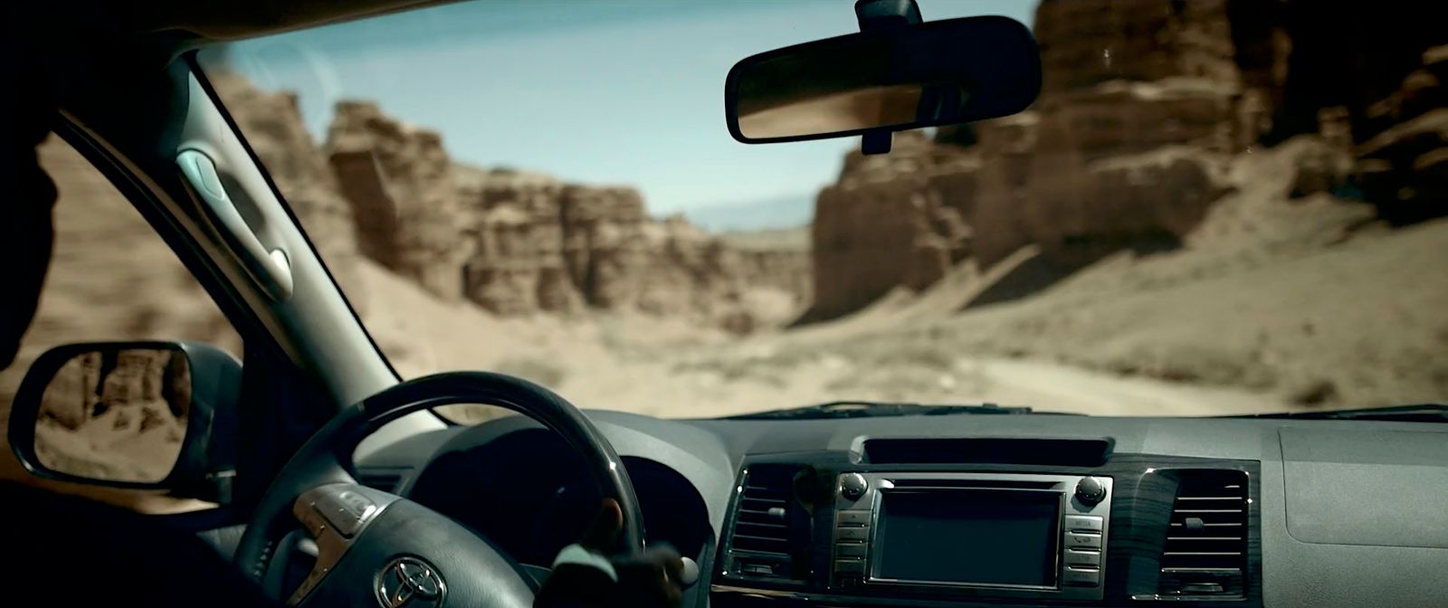 a car driving down a desert road with mountains in the background