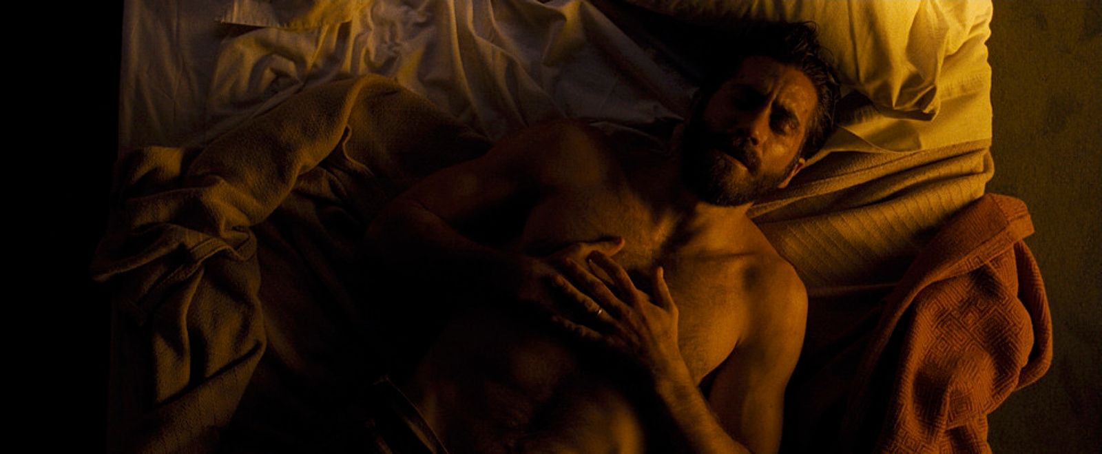 a shirtless man laying in bed under a blanket