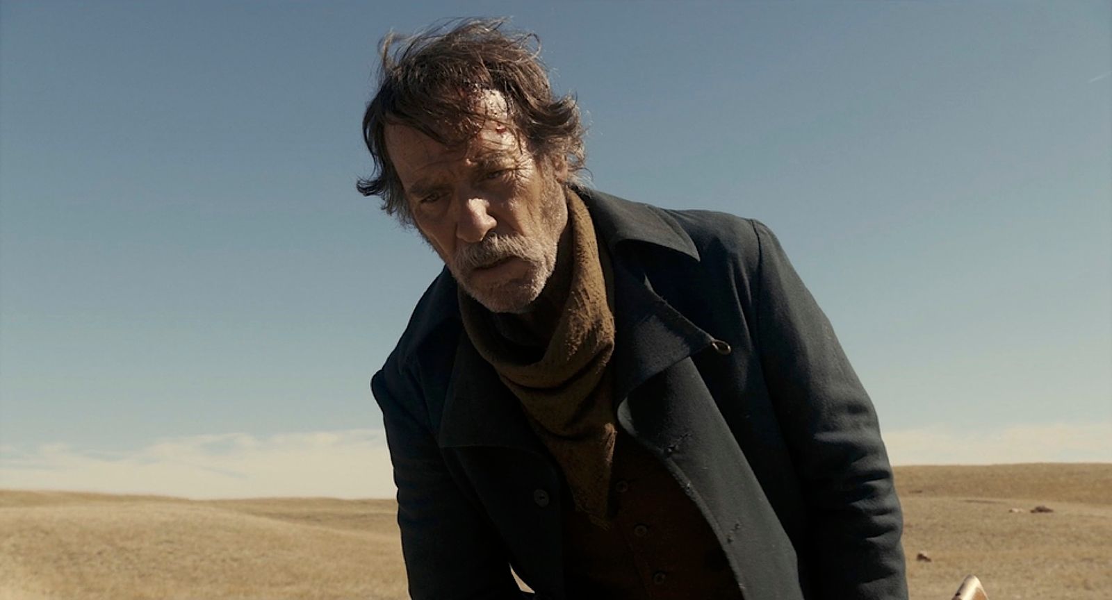 a man in a black coat and scarf standing in a desert