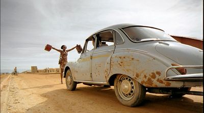 a man standing next to an old car on a dirt road