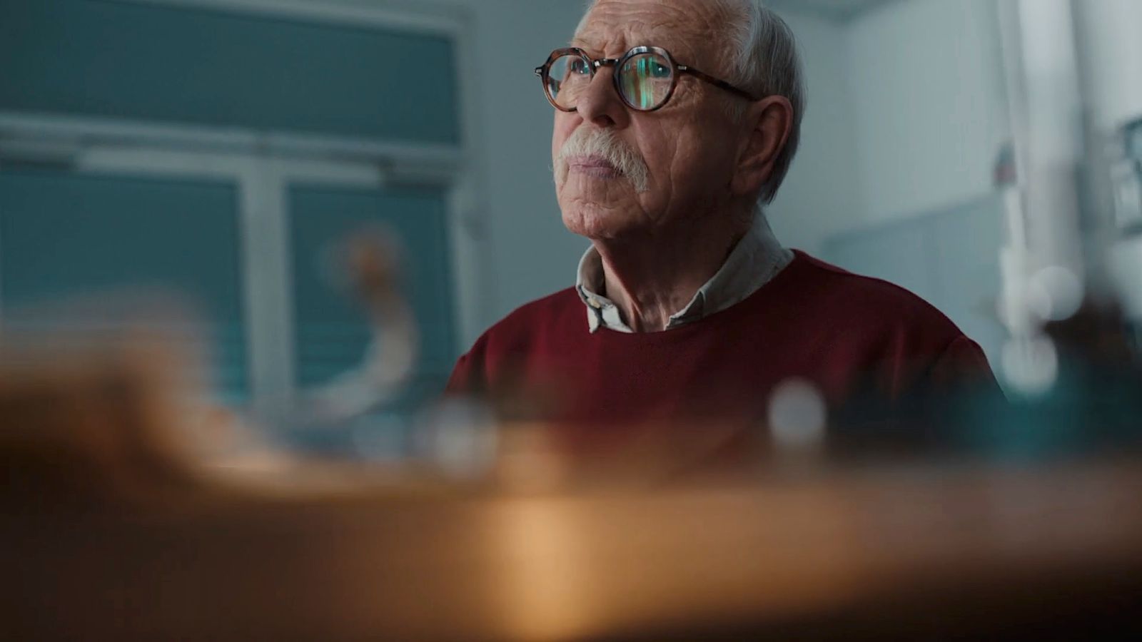 an older man with glasses sitting in a room