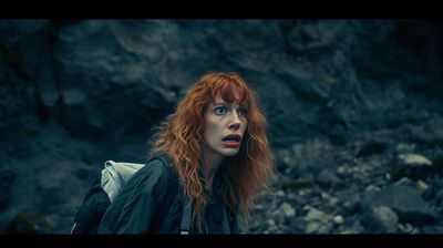 a woman with red hair standing in front of a mountain