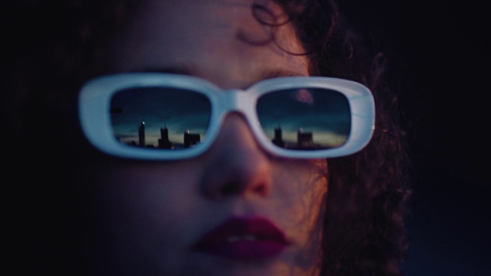 a woman wearing sunglasses with the reflection of a city in them