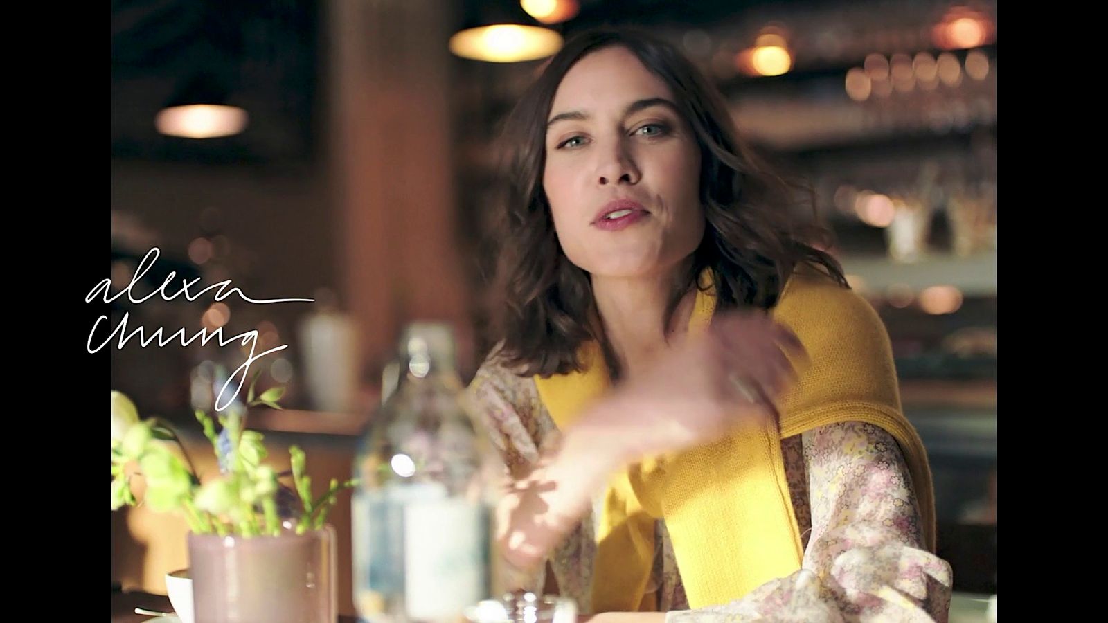 a woman sitting at a table with a bottle of wine