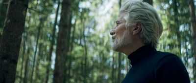 a man with white hair and beard standing in a forest